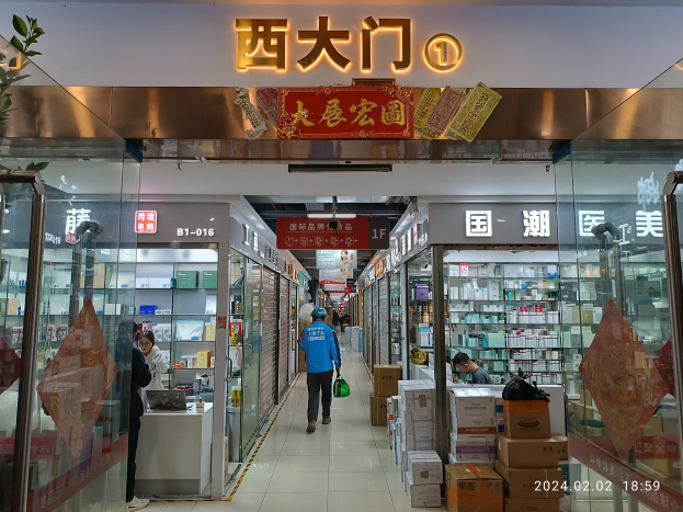 Innenraum einer chinesischen Apotheke mit Glaswänden, einer Pflanze links, Regalen mit Gegenständen, verstreuten Kartons und einem Namensschild oben, das auf eine chinesische Drogerie hinweist.