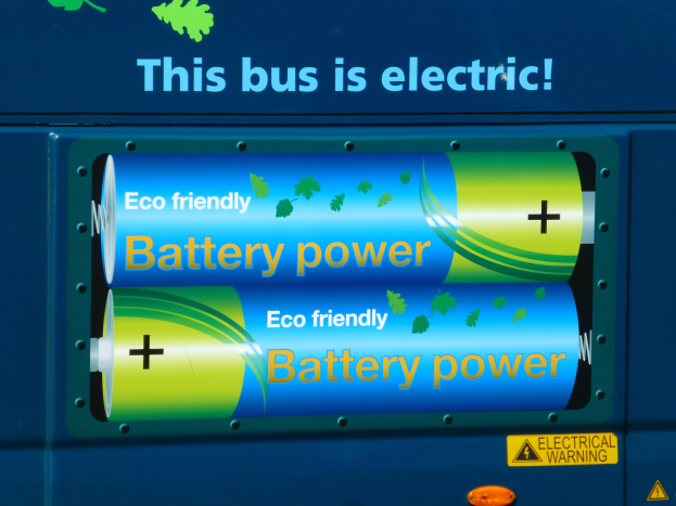 Blauer elektrischer Bus mit "Dieser Bus ist elektrisch"-Schild und zwei sichtbaren Batterien an der Seite.