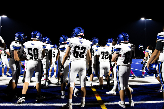 Eine Gruppe von Fußballspielern in Helmen und Stiefeln auf einem Feld unter Flutlicht, bereit für ein Spiel.
