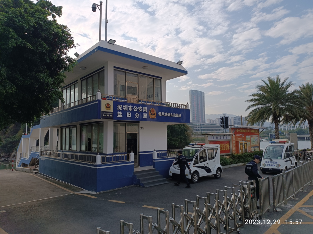 Blau-weißes Gebäude als Hongkonger Polizeiwache mit einem vor dem Gebäude geparkten Polizeiwagen identifiziert, umgeben von Fahrzeugen, Passanten, einem Geländer, Bäumen, anderen Gebäuden und einem bewölkten Himmel.