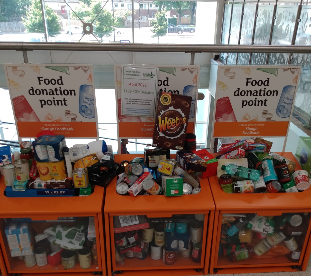 Orange Schränke mit Lebensmittelvorräten wie Flaschen, Dosen und Kartons, mit Informationsschildern und einem Blick auf Fahrzeuge, Bäume, Gebäude und Himmel durch Glasfenster.