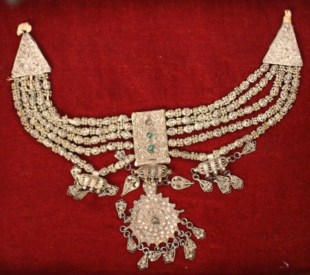 Silbernes Collier mit Smaragden und Diamanten auf rotem Samt-Hintergrund.