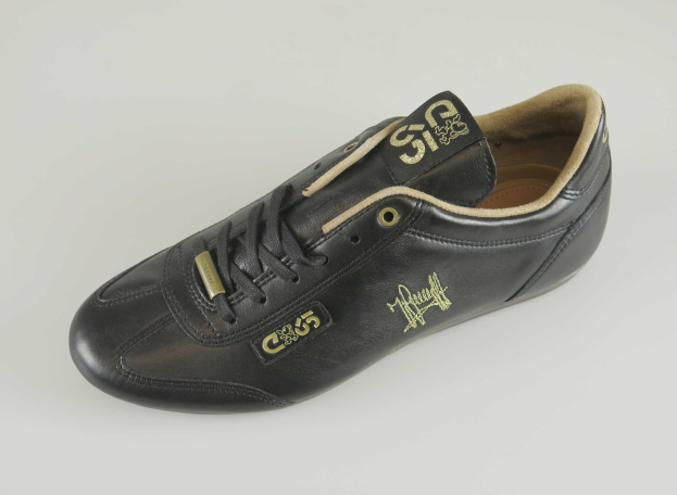Schwarzer Lederschuh mit goldenem Logo auf der Seite, auf einem weißen Hintergrund, mit einem schlanken Design und einem glänzenden Finish.