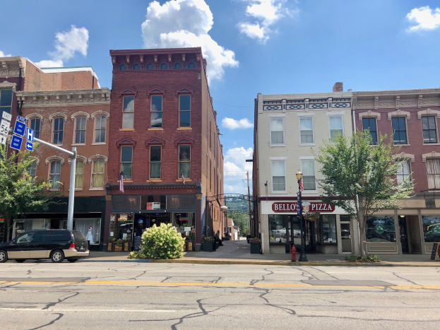 Eine Stadtstra├če mit parkenden Autos, Geb├Ąuden, B├Ąumen, Laternen, Schildern und einem Feuerhydranten unter einem bew├Âlktem Himmel, die ein kommerzielles Eigentum repr├Ąsentiert.