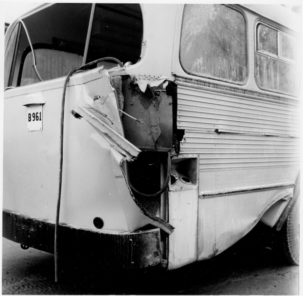 Schwarz-weißes Foto eines Busses mit schwerer Frontschäden durch einen Autounfall auf der Straße.