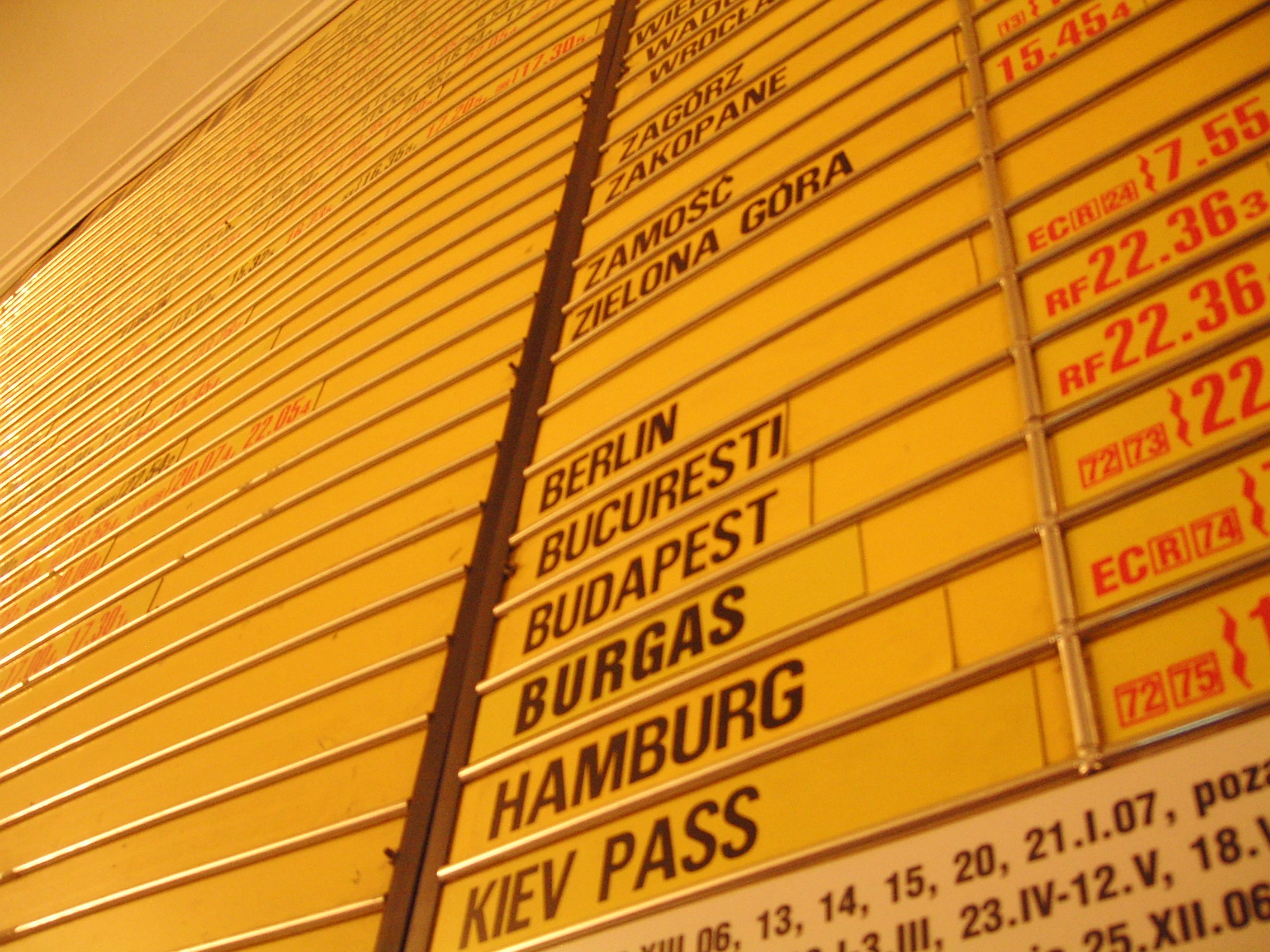 Gelbe Wand mit mehreren gelben Schildern, die wahrscheinlich Abfahrts- und Ankunftszeiten für verschiedene Ziele angeben.
