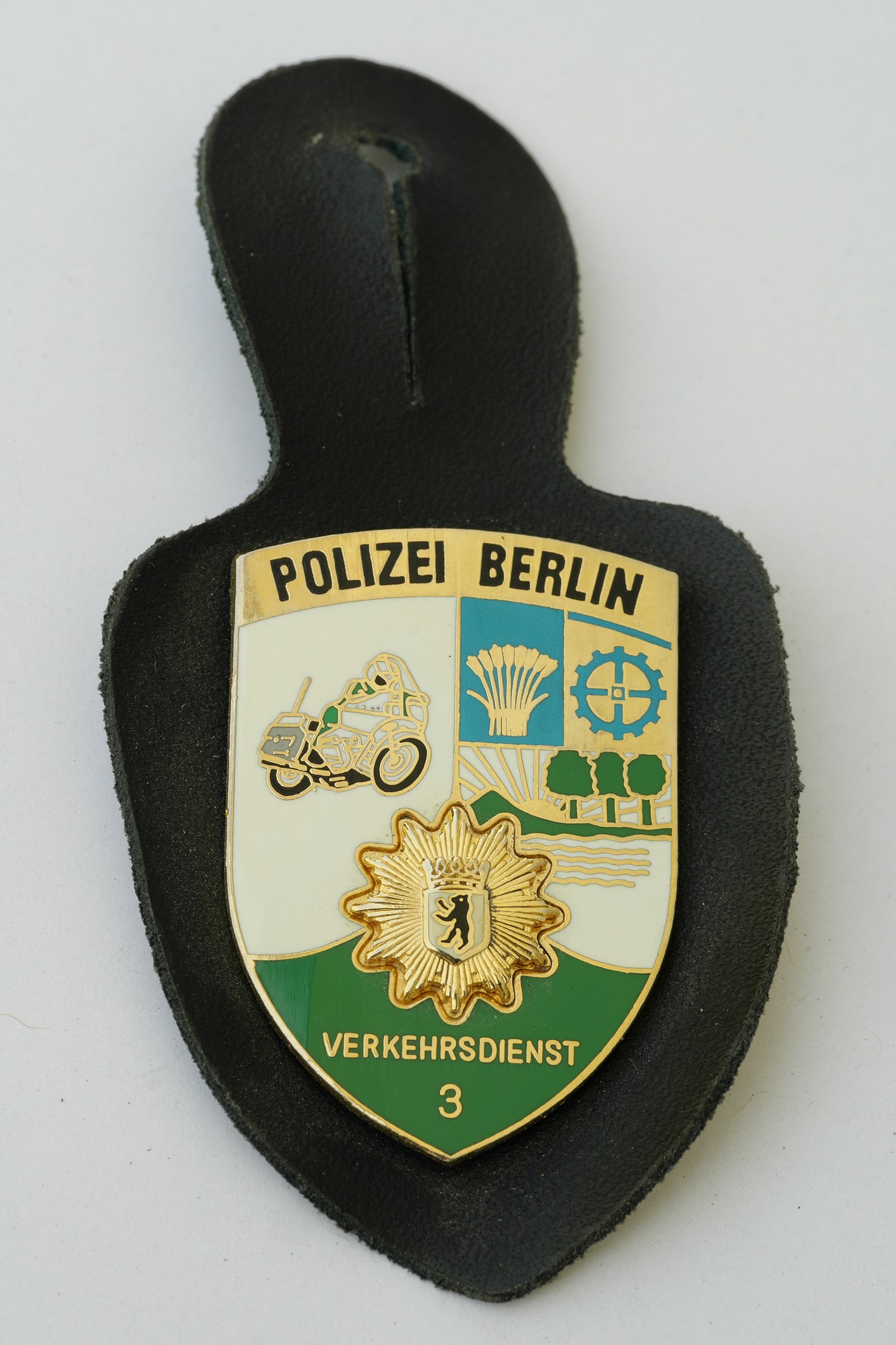 Ein schildförmiges Polizeibadgeb mit 'Polizei Berlin' in fetter schwarzer Schrift auf einem blauen Hintergrund mit einem weißen Stern und Rahmen, das auf einer Oberfläche liegt.