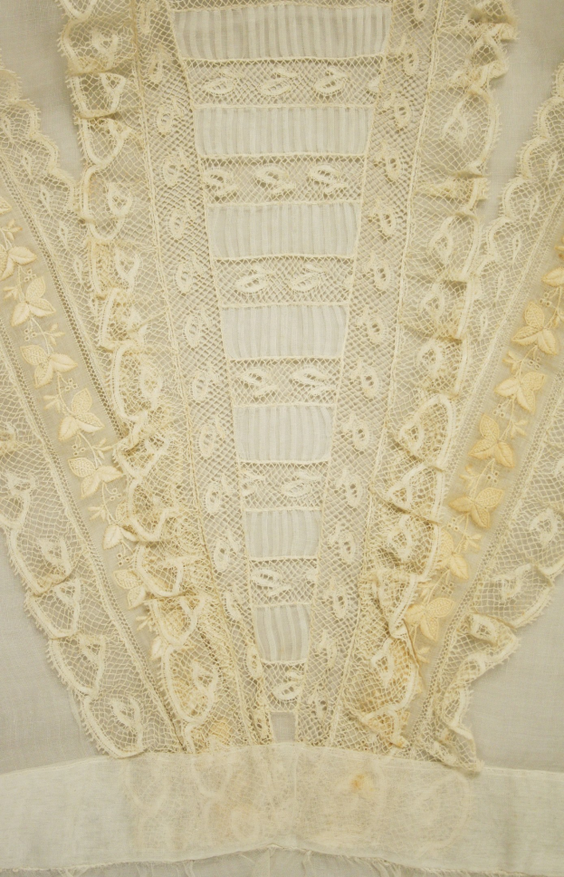 Nahaufnahme eines weißen Kleides mit zarter, detailreicher Spitzenverzierung auf einem leichten, luftigen Stoff.