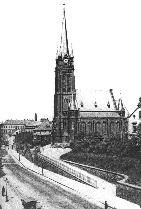 Schwarzes und weißes Foto einer Stadtstraße mit St. Peter's Church im Hintergrund, gesäumt von Gebäuden, Bäumen, Fahrzeugen und einigen Fußgängern.