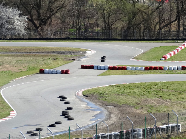 Rennstrecke mit zahlreichen gestapelten Reifen an den Seiten, umgeben von Gras und Maschendrahtzaun, mit Bäumen im Hintergrund.