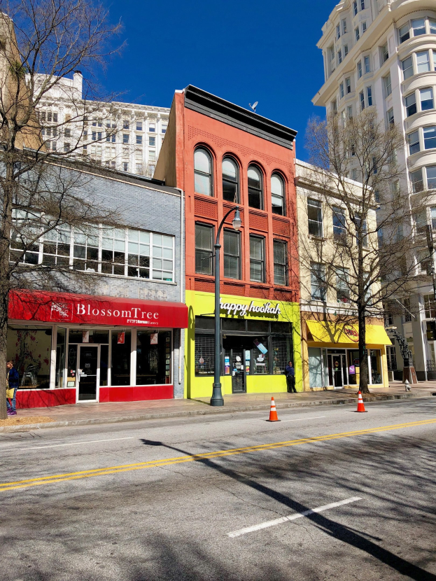 Eine Stadtstraße im Zentrum von Portland mit hohen Gebäuden, Fahrzeugen, Fußgängern, Verkehrskegeln, Straßenlaternen und Bäumen unter einem bewölkten Himmel.