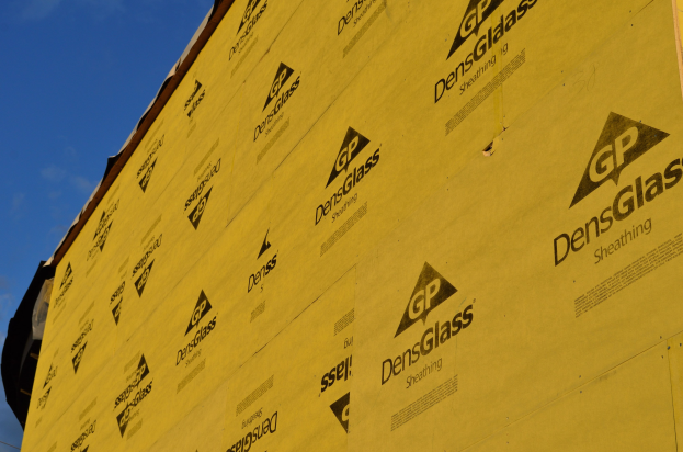 Gelbe Isolierung bedeckt die Seite eines im Bau befindlichen Gebäudes gegen einen Himmel mit weißen, flauschigen Wolken.