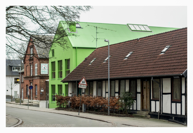 Eine Reihe von Häusern mit grünen Dächern, die eine Straße säumen, mit Straßenlaternen, Schildern, Büschen, Bäumen und einem klaren blauen Himmel.