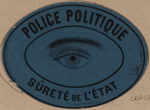 Brauner Karton mit einem blauen Aufkleber mit der Aufschrift "Polizei Politique Surete de L'Etat" und einem Augensymbol.