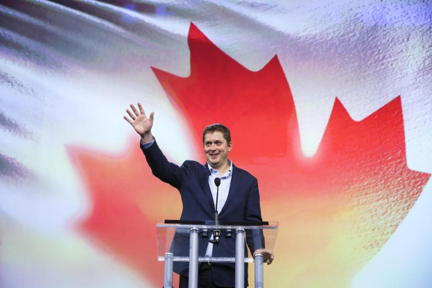 Der kanadische Premierminister Alex Salmond steht an einem Podium mit Mikrofonen, lächelnd vor einer kanadischen Flagge, mit einem sichtbaren Bildschirm im Hintergrund.