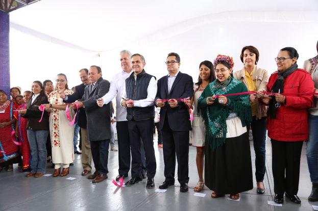 Eine Gruppe von Menschen bei einer Scherenschnitte-Zeremonie, die lächeln und Scheren halten, mit Papieren auf dem Boden und einem weißen Tuch im Hintergrund.