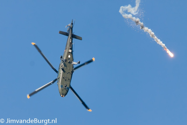 Militärhubschrauber startet eine Rakete, emitiert Rauch und Feuer, steigt in den Himmel auf mit Text in der linken unteren Ecke.
