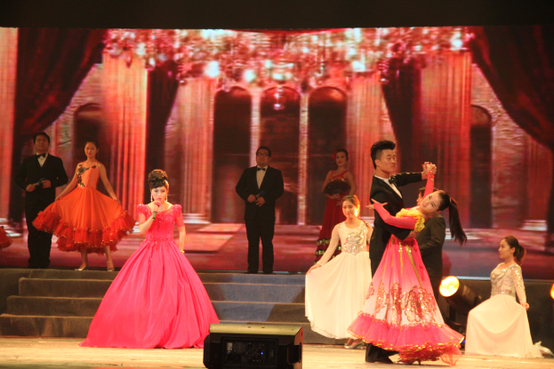 Eine Gruppe von Menschen auf einer Bühne mit Lichtern, Stufen und einem Hintergrundbild, mit einem Lautsprecher unten, was eine Tanzvorstellung suggeriert.