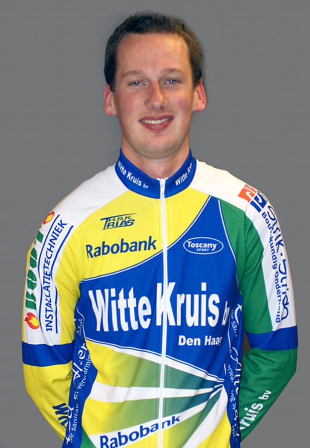 Ein männlicher Sportler posiert für ein Foto, trägt ein Shirt mit mehreren Sponsorenlogos.
