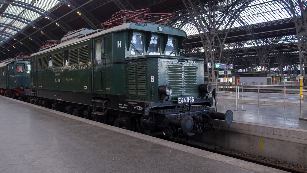 Ein Zug auf Schienen mit Geländern und Brettern im Hintergrund, Lampen auf dem Dach und Himmel darüber, mit einem Boden darunter.