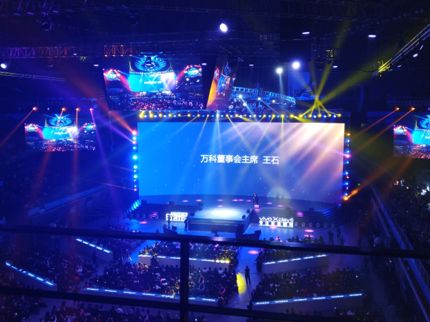 Eine große Menschenmenge vor einer hell erleuchteten Bühne mit Metallabsperrungen, die auf ein Esports-Event warten