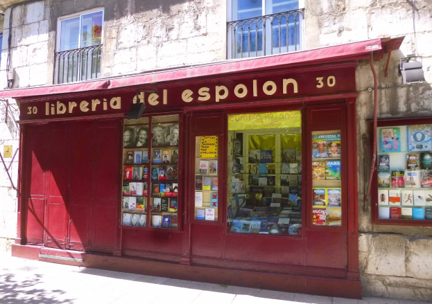 Eine Buchhandlung mit rotem Schirm namens "Libreria del Espolon" mit ordentlich angeordneten Büchern, die durch ihre Fenster sichtbar sind.