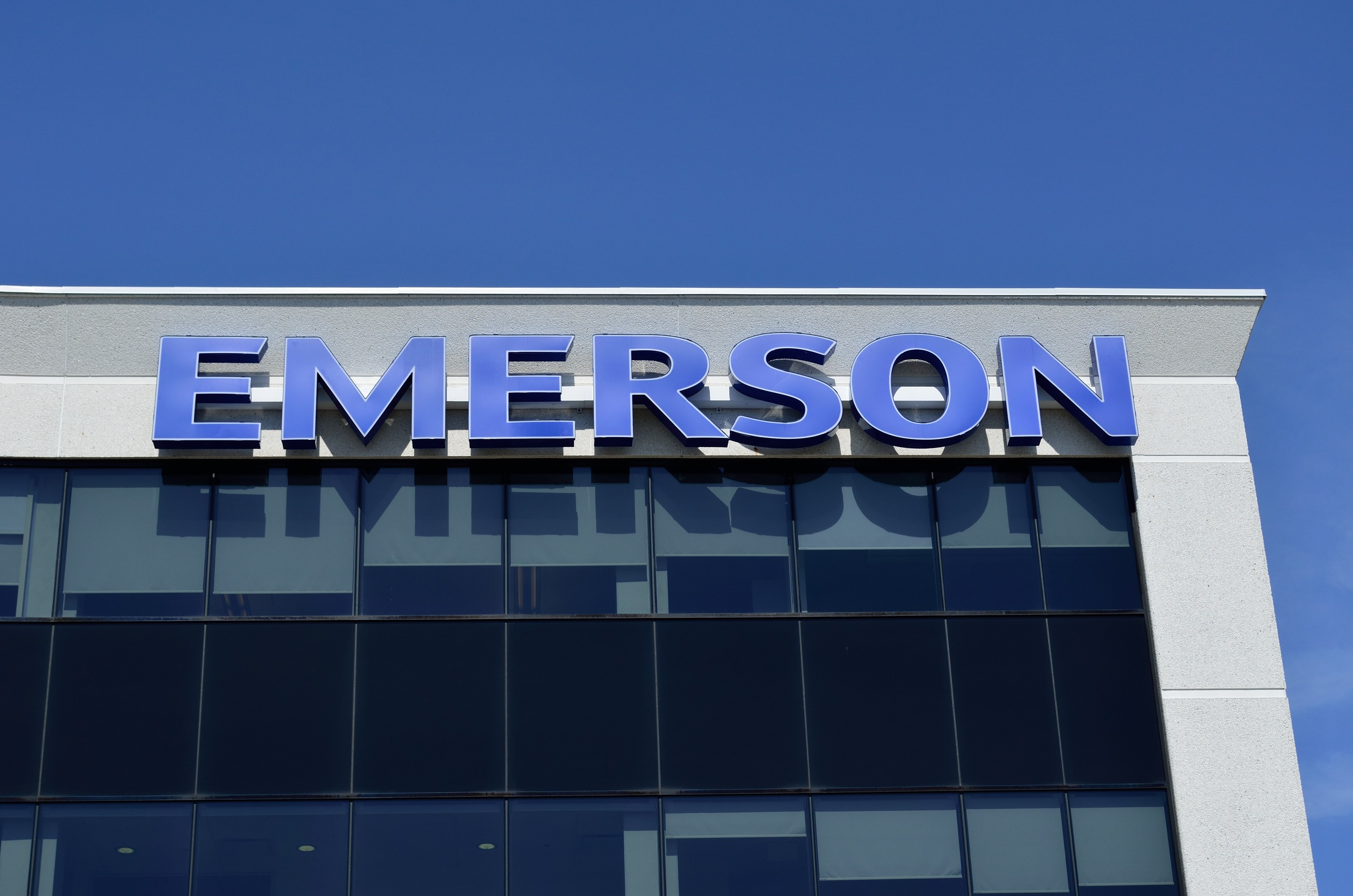 Emerson-Logo an einer Gebäudefassade mit dem Text "Emerson investiert $1,5 Milliarden in den USA" vor einem klaren blauen Himmel.