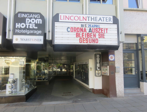 Außenansicht des Lincoln Theaters in Berlin, Deutschland, mit Glasfenstern und -türen, einem Schild mit Text und einer belebten Stadtlandschaft im Inneren.