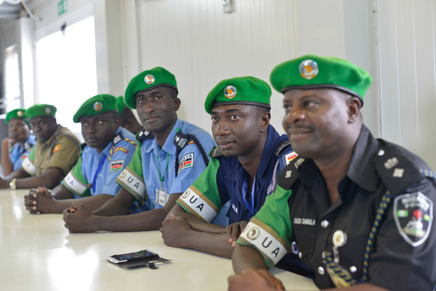 Eine Gruppe von Polizeibeamten sitzt an einem Tisch während einer Schulung, mit Mobiltelefonen und anderen Gegenständen auf dem Tisch, in einem Raum mit Fenstern und Deckenleuchten.
