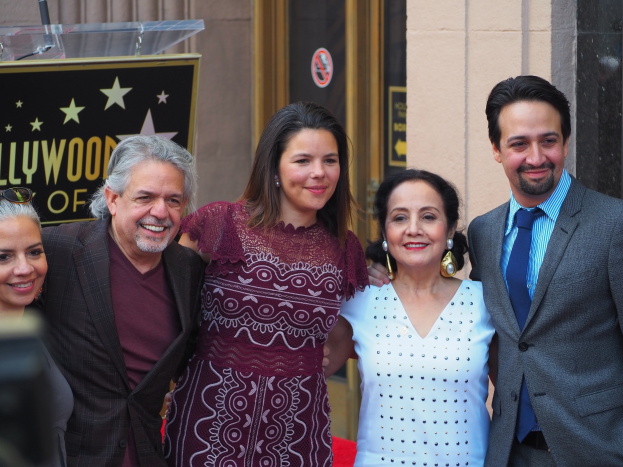 Gruppe von Menschen auf einem roten Teppich bei der Zeremonie des Hollywood Walk of Fame, mit einer Kamera auf der linken Seite und einer Tafel, einem Podium und einer Wand im Hintergrund.