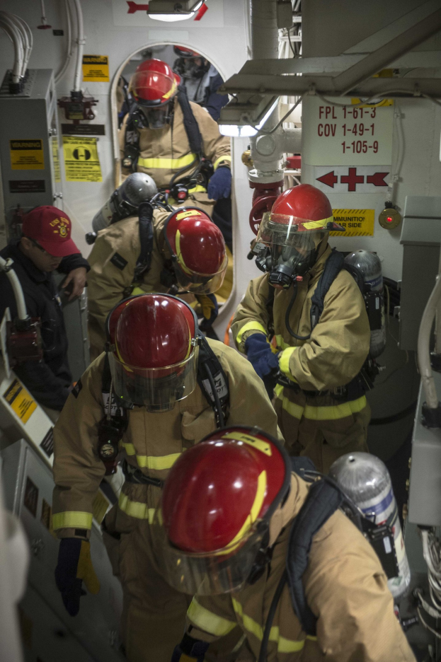Feuerwehrleute in Schutzausrüstung arbeiten an einem Boot mit Rohren und Plakaten im Hintergrund.