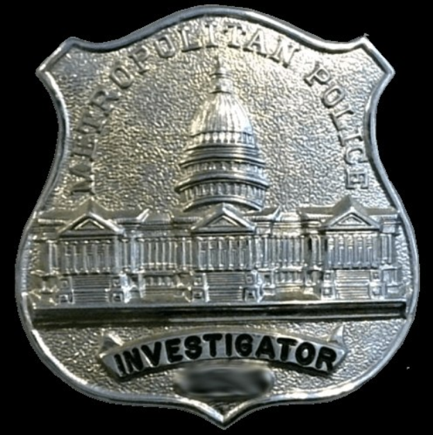 Ein silbernes Polizeischild mit der Aufschrift "Ermittler" auf einem weißen Hintergrund.