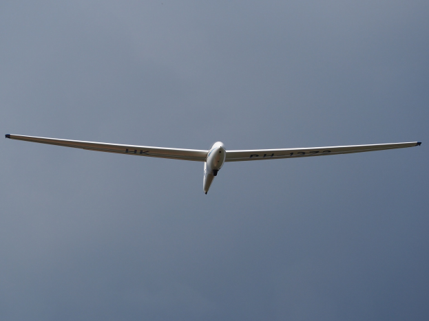 Ein kleines weißes Einmotoriger Segelflugzeug mit ausgebreiteten Flügeln durchquert einen hellblauen Himmel bei starker Sonneneinstrahlung.