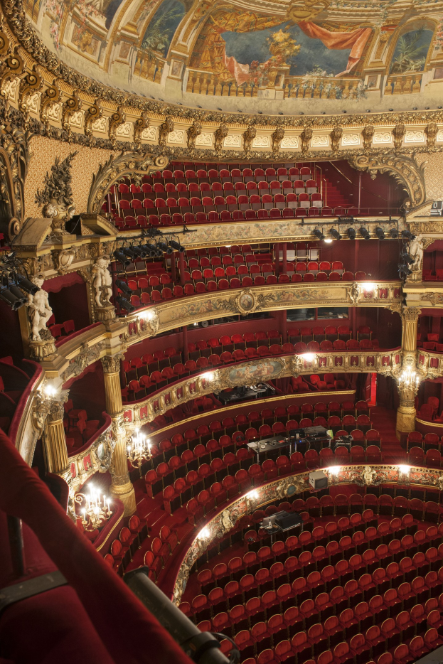 Innensicht des Auditoriums der Royal Opera House in London mit Sitzreihen, verzierten Geländern, Säulen, Wandskulpturen, Deckenlüstern und einem großen Deckengemälde.