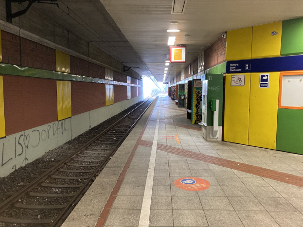Ein Bahnsteig in Berlin Hauptbahnhof, Deutschland, mit einem Zug auf den Schienen, beleuchtet von Deckenlampen, einer graffitibedeckten Wand auf der linken Seite und ein paar Gegenständen auf der rechten Seite.