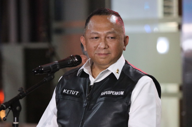 Ein Mann in einer schwarzen Weste und einem weißen Hemd steht an einem Mikrofon und sieht besorgt aus, mit einem unscharfen Hintergrund.