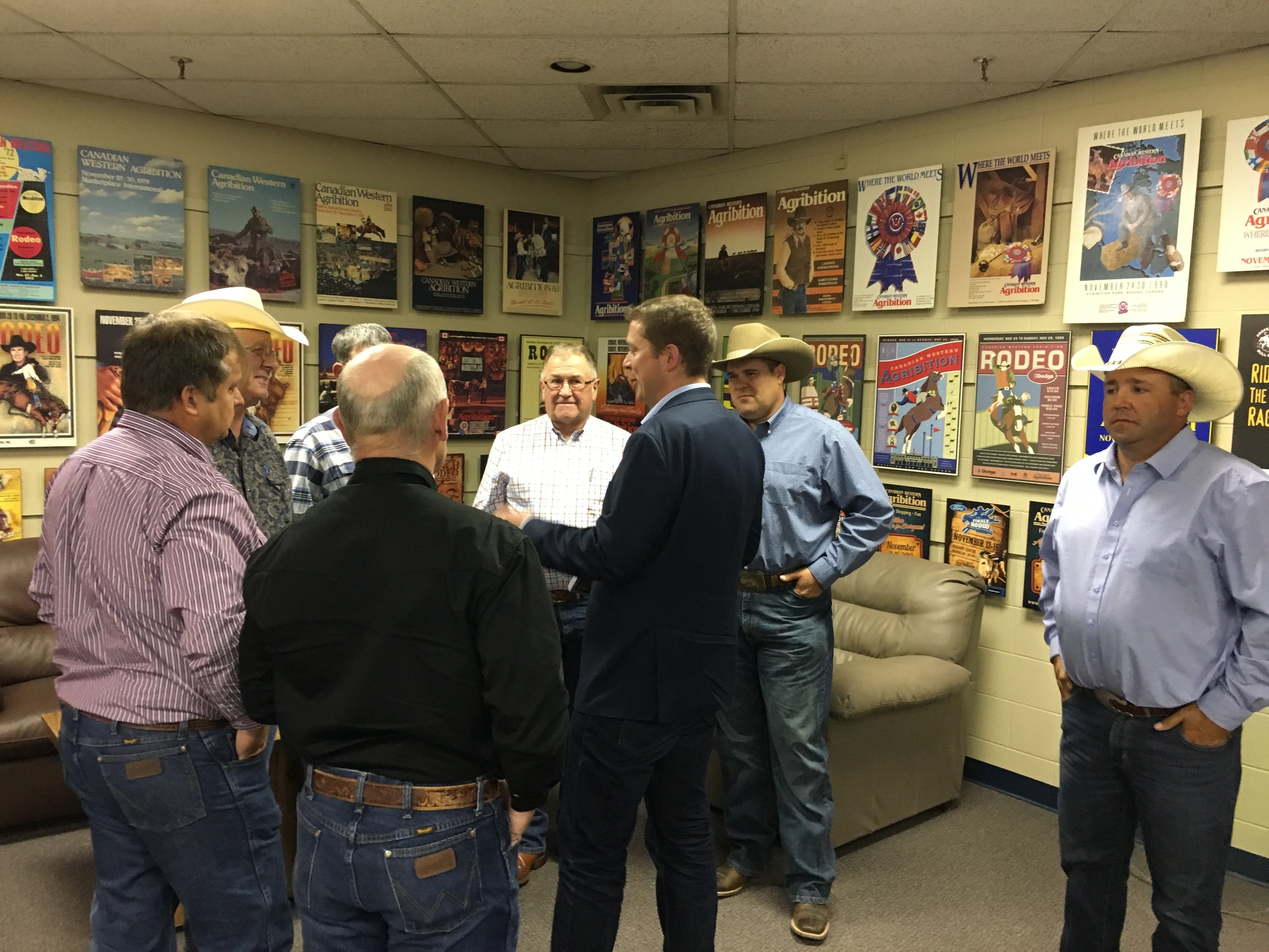 Gruppe von Männern in einem Raum mit Sofas, Plakaten an den Wänden und Deckenlampen, die sich unterhalten.
