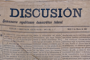 Ein gelblich, leicht zerknittertes Zeitungsblatt mit der schwarzen Schrift 'Diskussion', das die Schlagzeile 'Semanario Repúblicano Democrático Federal' trägt.