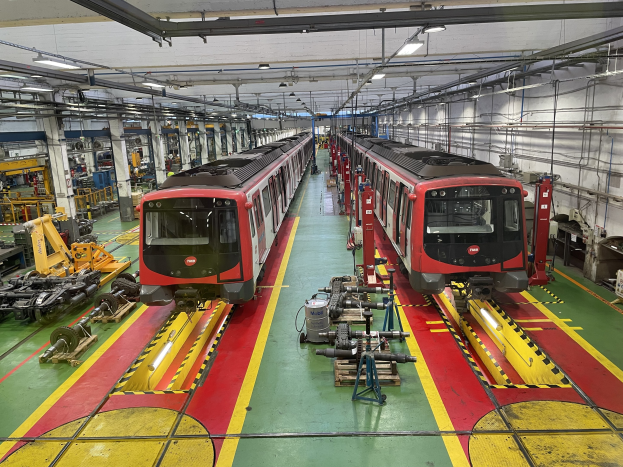 Zwei Züge auf den Schienen in einer Daimler Group-Fabrik mit Maschinen und Rohren an der rechten Wand.