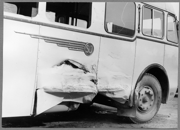 Schwarzes und weißes Foto eines verunglückten Busses mit eingedellter Front, zersplitterten Fenstern und ge├Âffneter Fahrertür.
