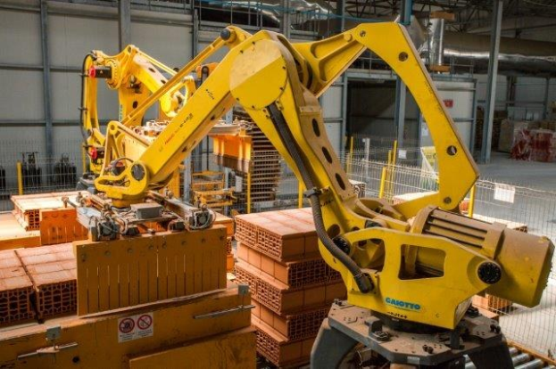 Ein große Lagerhalle voller numerous Kartons, Kräne, ein Zaun, Masten und andere industrielle Ausrüstung, mit einer Wand im Hintergrund.