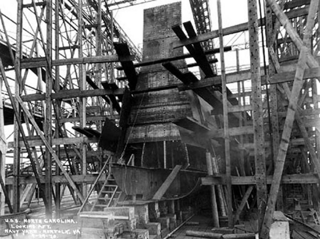 Schwarzes und weißes Foto eines Schiffs in einem Schiffbau, mit hölzernen Pfählen und Treppen im Vordergrund und Himmel im Hintergrund, mit Text "Marinebewaffnung" in der linken unteren Ecke.