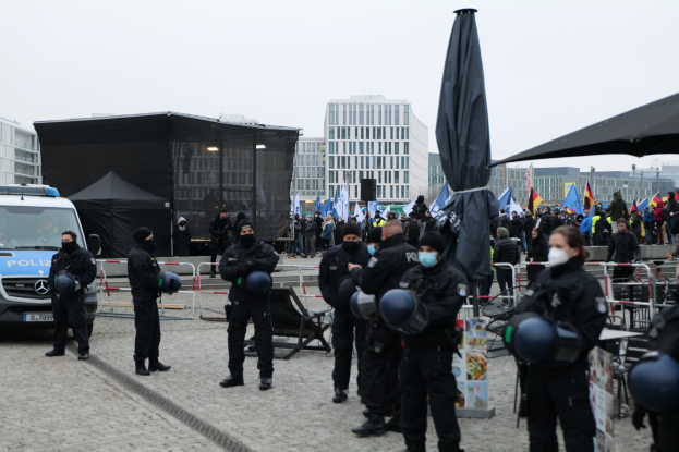 Polizeibeamte in Uniform hinter Barrieren vor einer Menge von Demonstranten, einige mit Helmen und Masken, mit Zelten, Fahnen und Gebäuden im Hintergrund bei einer Anti-Austeritäts-Demonstration in Berlin.