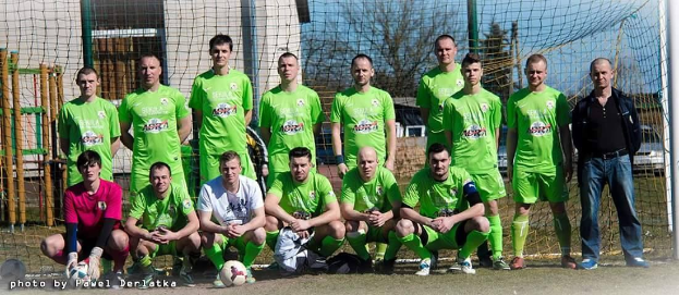 Eine Gruppe von Männern in grünen T-Shirts steht auf einem Fußballfeld, einige hocken, mit einem Ball und einem Torpfosten.