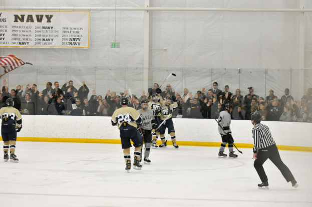 Gruppe von Menschen, die Eis-hockey auf einem Eisstadion spielen, mit Zuschauern auf den Tribünen, die Helme tragen und Hockey-Schläger halten, mit einer Wand im Hintergrund und einer Fahne links.