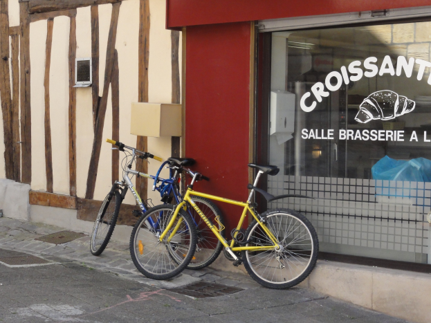 Zwei Fahrr├Ąder nebeneinander auf einem Gehweg vor einem Laden mit einer Glaswand mit Text und einem Objekt links von den Fahrr├Ądern.