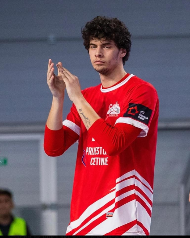 Ein Mann in einem roten und weißen Hemd klatscht in der Vordergrund mit einer anderen Person und einer Wand im Hintergrund, Text unten lautet 'Kopenhagen Futsal Club - Foto 1'.