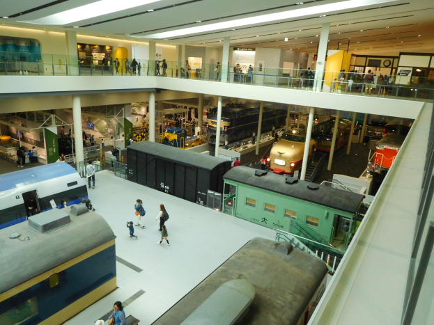 Ein gro├če Museumshalle mit verschiedenen Zugtypen, Menschen, Gel├ädern, S├Ąulen, Lichtern und Informationsschildern.