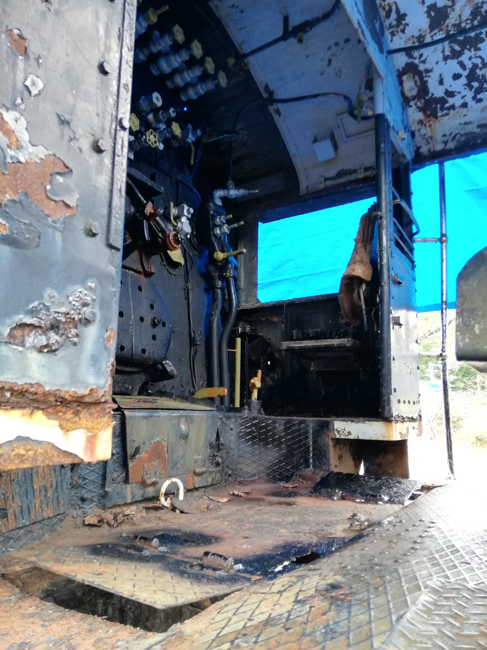 Das Innere eines verrosteten, baufälligen Lastwagens mit sichtbaren Gebrauchsspuren, vor Bäumen und einem klaren blauen Himmel.
