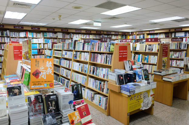 Ein gut organisierter Buchladen mit Regalen und Tischen voller Bücher, Informationsschildern auf dem Boden und Deckenlampen.